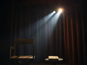 Otwarty, postarzany scenariusz z odręcznymi notatkami leżący na oświetlonej deskach sceny teatralnej.